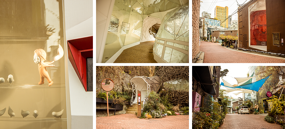 Left picture: A doll-shaped figure dressed in a landing suit; top-middle picture: A seemingly octogonal-shaped corridor with a brown walkway; bottom-middle picture: An entrance surrounded in vegetation with a round mirror and entrance sign on either side; top-right picture: The brick walkway winding at the far corner with a large exhibition poster up on the building to the right; bottom-right picture: Vegetation surrounding each building in site with some blue, white, and green kite-looking canopies hanging over the brick walkway