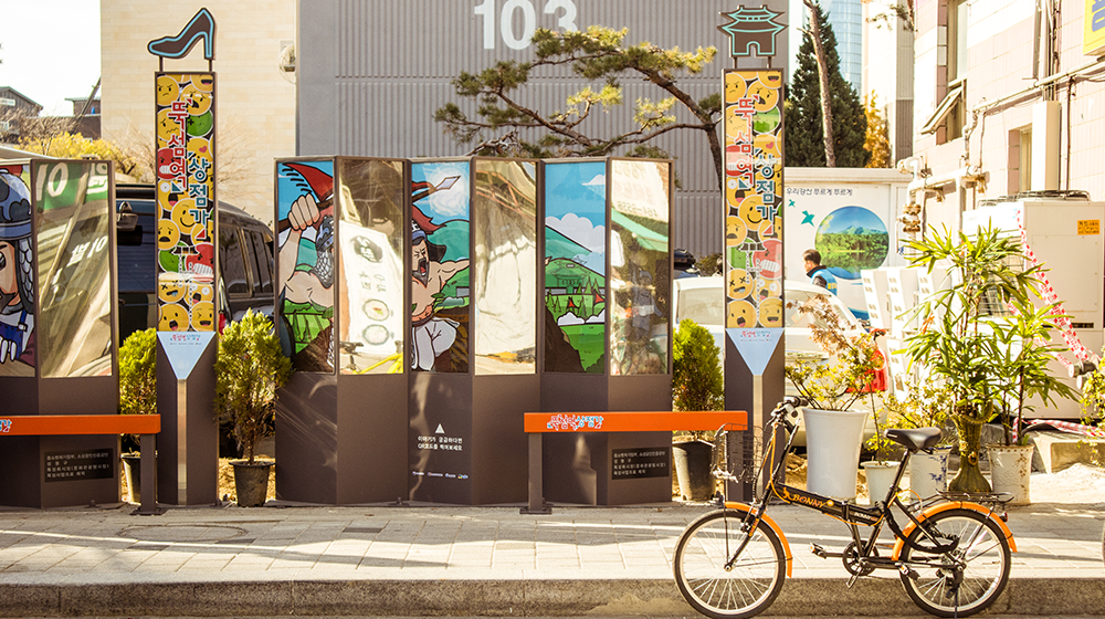 A sidewalk with a parked bike out front and some brown bulletin structures on display with illustrations on them