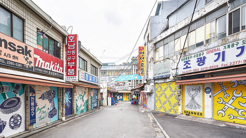 An alleyway in Euljiro during the off hours of neighborhood businesses with the lowered metal doors of each store offering a different design symbolizing their specialization