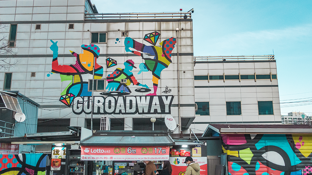 Guroadway drawing up on the building with a colorful drawing of street performers and a lottery shop streetside store during business that advertises having sold winning tickets to 6 1st place winner and 17 2nd second place winners during their tenure