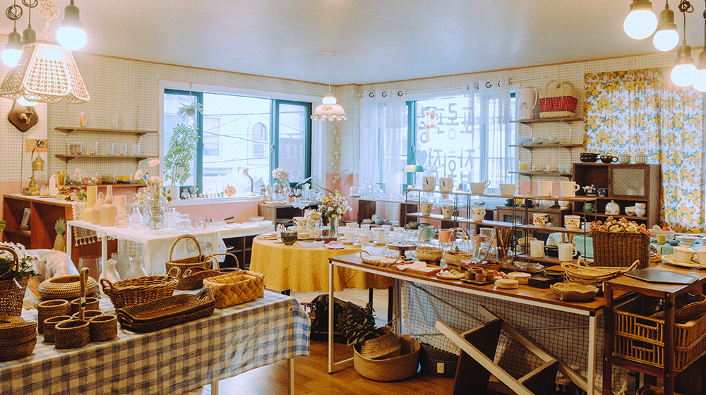 Store interior showing all the different baskets, dishes, cups, glasses, shelving, and more, with the windows in the background covered by floral curtains