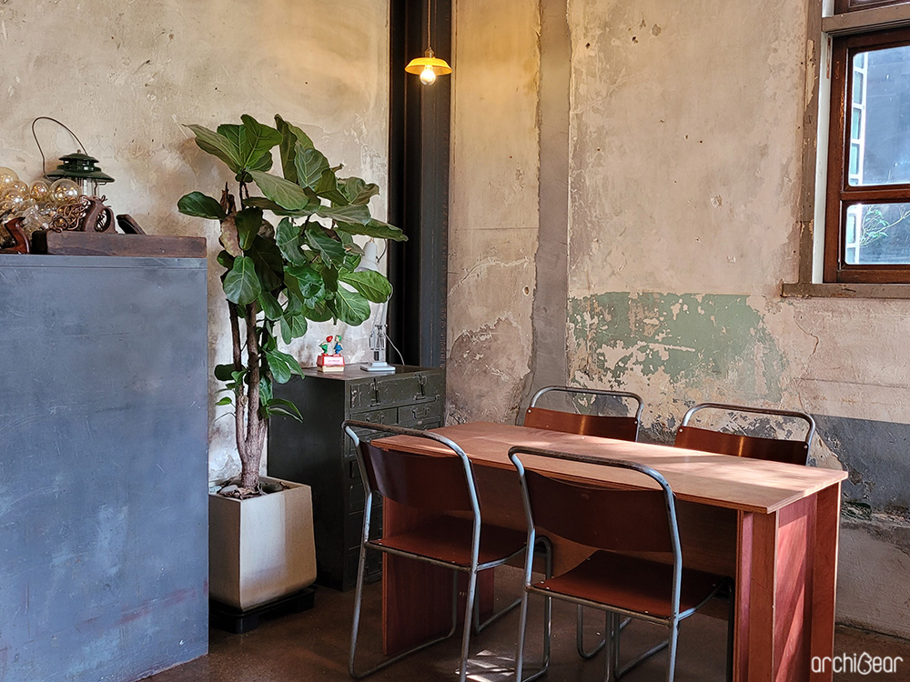 Chairs are placed in front of a vintage table, and a potted plant with pretty green leaves is in front of the wall. The vintage walls add to the charming interior.